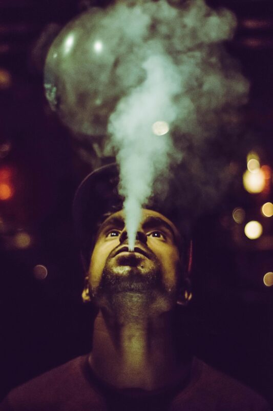 A man exhaling smoke, showcasing a Packwoods x Runtz disposable vape in his hand.